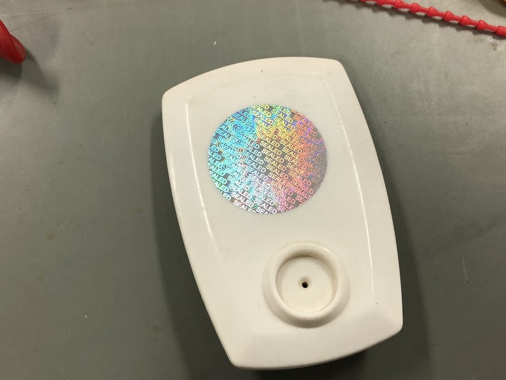Tamper evident holographic label attached to a plastic device